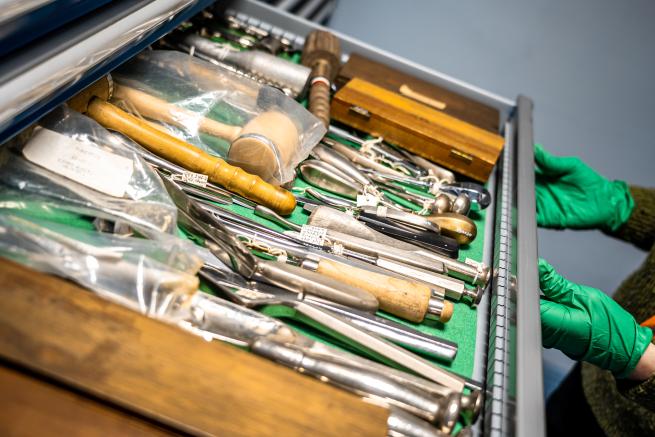 Two gloved hands opening a drawer of surgical equipment