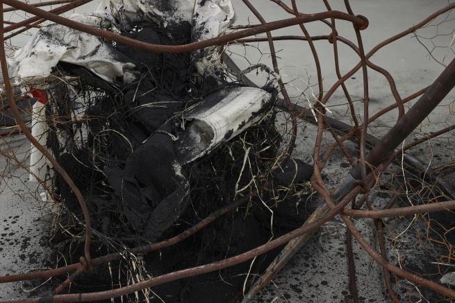 Detail of an abstract sculpture, with burned materials and rusty chicken wire at the centre, with rusted metal bars bent around it.