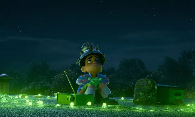 Elio sits looking concerned at the night sky, light from below by green lightbulbs.