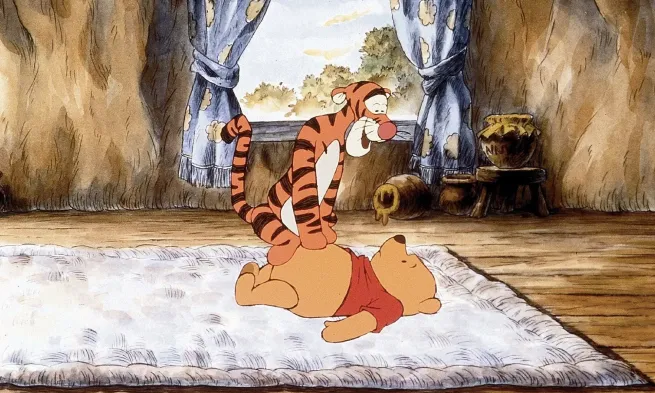 Tigger sits on Pooh's belly, looking down leefully at him whilst Pooh seems disconcerted.