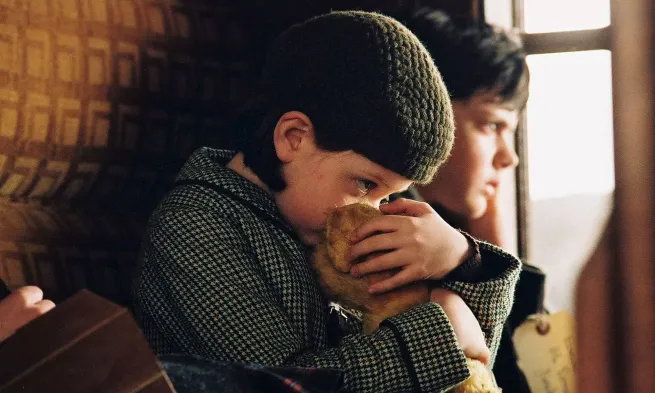 Two children sat in an old fashioned railway coach, during the blitz.