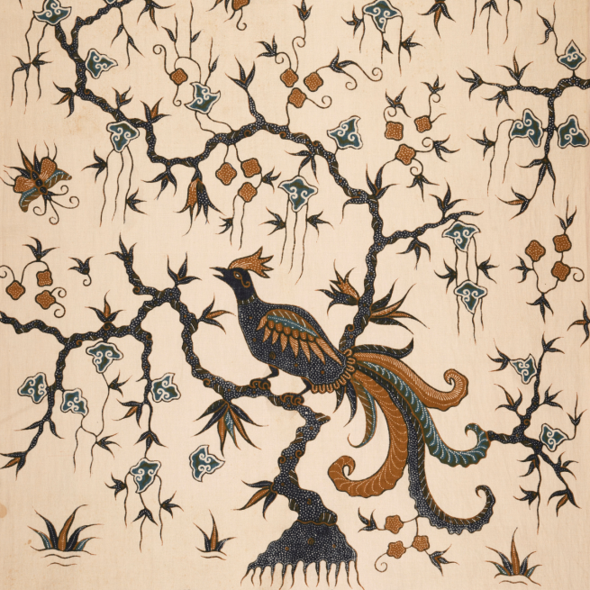 Section of a batik fabric with a design showing a blue and orange bird on a stylised branch surrounded by a blue and orange floral pattern, on a pale brown background.