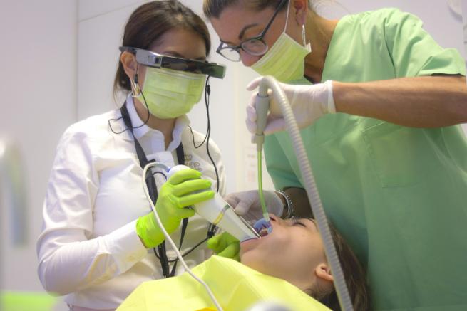 A patient in a dentist's chair with the dentist and assistant drilling a tooth
