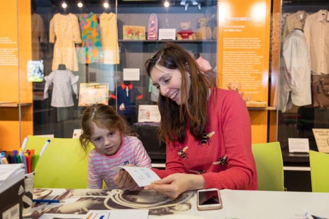 A woman and a child sit at a table in the M&S Archive exhibition, creating something crafty