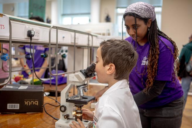 A volunteer helps a child look through a microscope