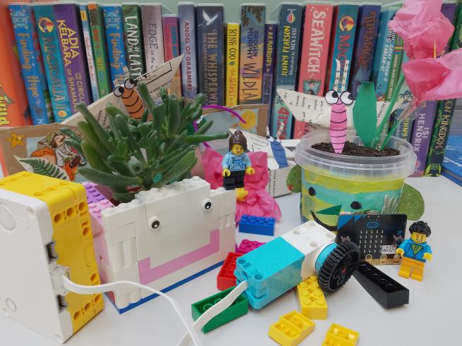A Lego cube with a pot plant inside and a Lego Spike motor and hub, plus a plant pot with collage on it