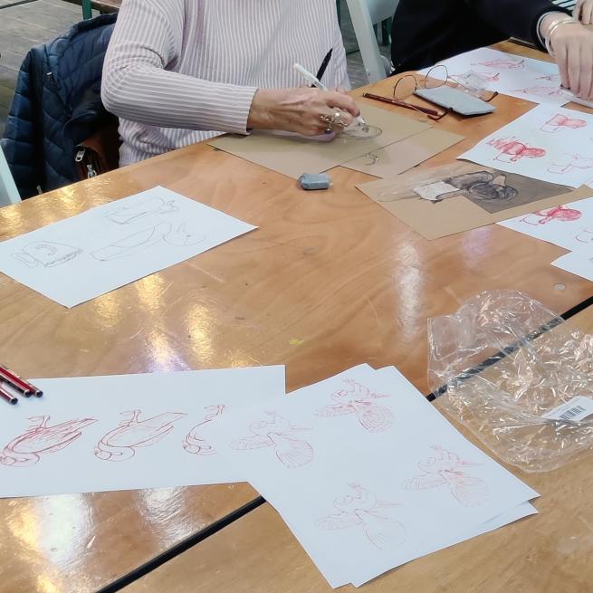 Some drawings of birds laid on a table and a womans hand holding a pencil in the background