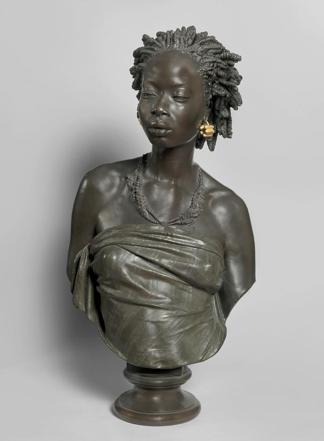 A statue of a striking black woman, her body draped in cloth with a bright golden earring 