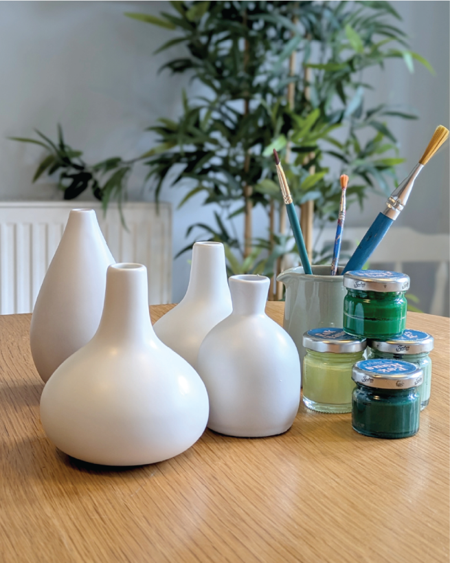 Plain white bud vases with pots of paints and brushes
