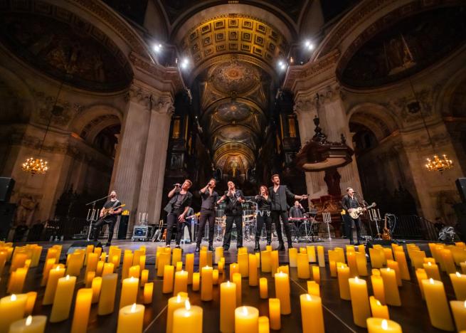 A cast of vocalists and full live band, surrounded by hundreds of candles, in a grand historic building.