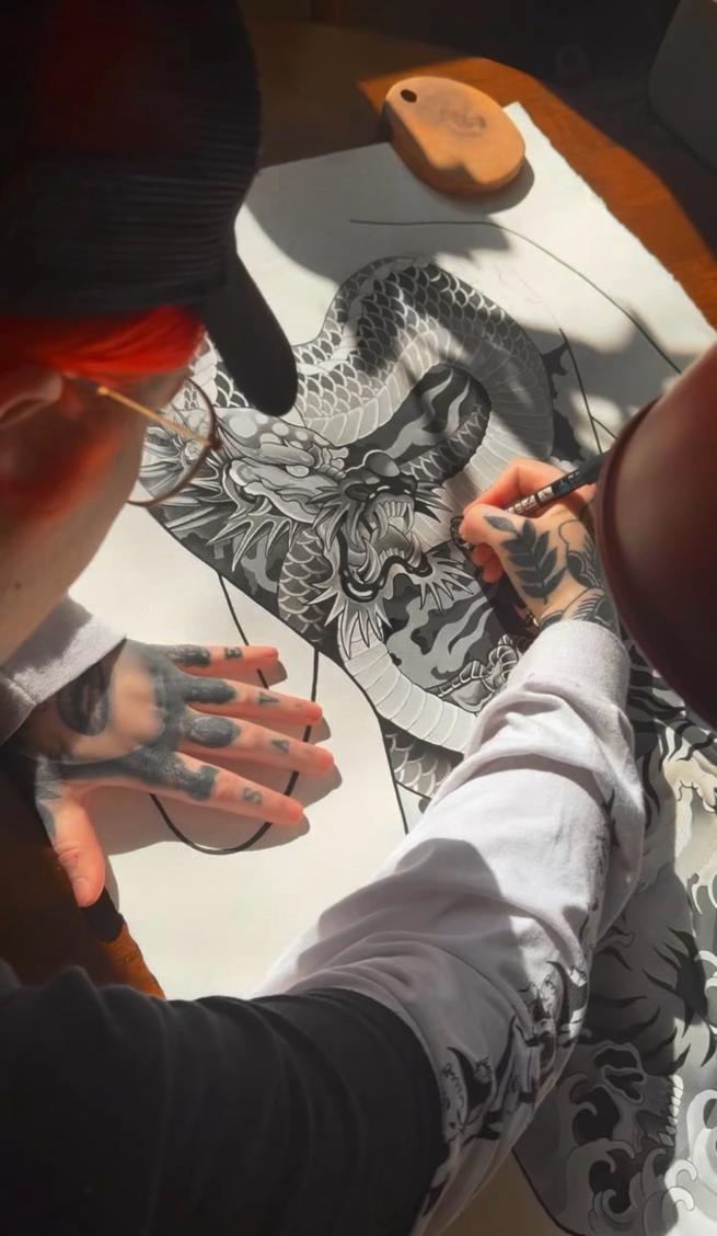 A photograph of an artist painting a dragon and tiger back piece tattoo design