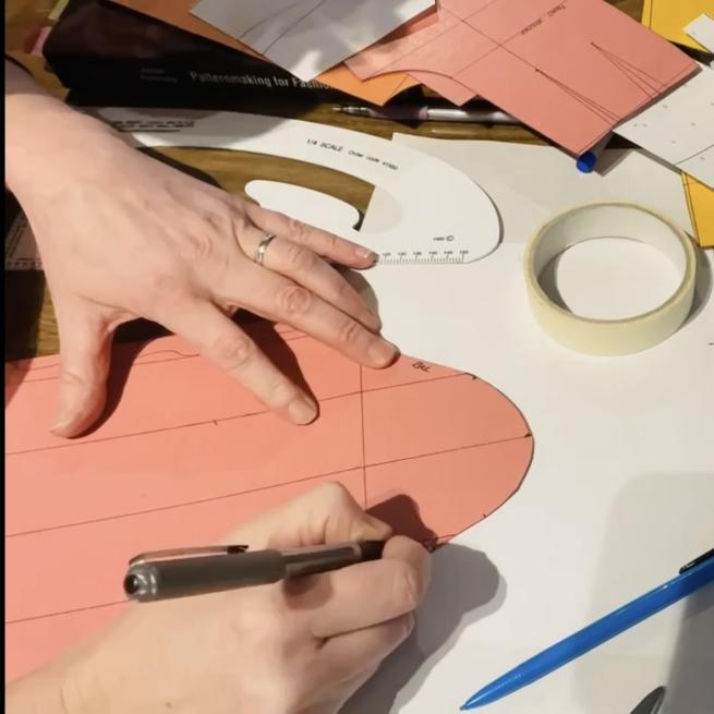 A hold holding a pen over a salmon coloured dressmaking pattern 