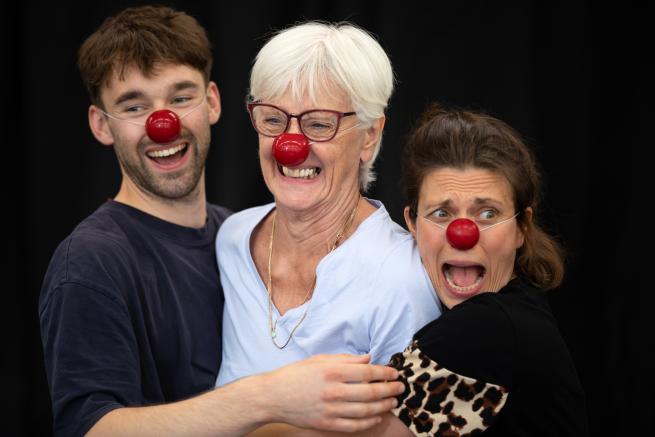 Three people wearing red clown noses with funny facial expressions