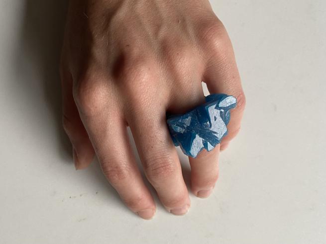 A large blue wax ring is worn on the ring finger of a person hand.