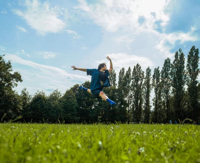 Boy leaping on grass with trees and sunny sky in the background
