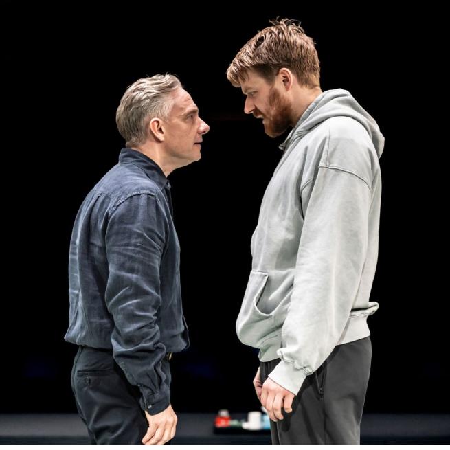 Against a stark black background, Martin Freeman and Jack Lowden stare at each other intensely on-stage.