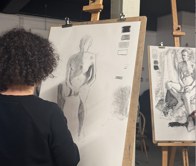 A person stood at an easel drawing a tonal study in charcoal of the life model 
