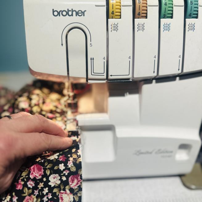 a hand guiding some flowery fabric through a sewing machine