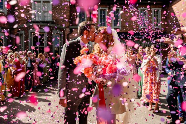 Wedding couple kissng in a spary of colourful confetti 