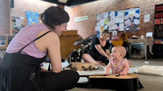 Chess of Empowered Sound smiling at a smiling baby playing with an acoustic guitar