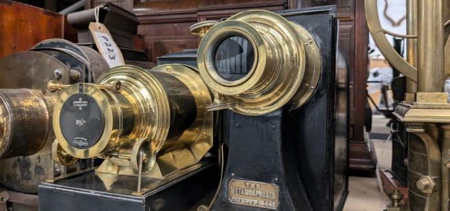 Three brass and wood lantern projectors sitting on a wooden shelf. 