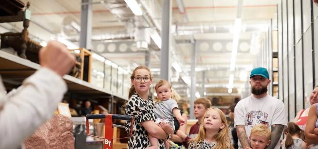 Family group standing in front of metal shelves with museum objects.  