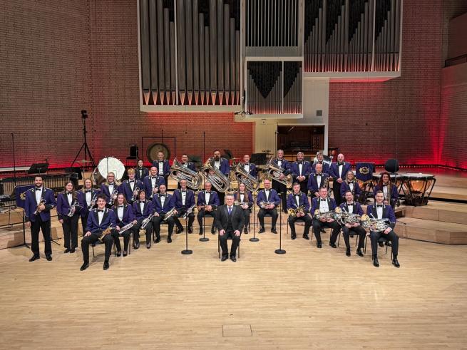 A brass band sat on a stage ready to perform. 