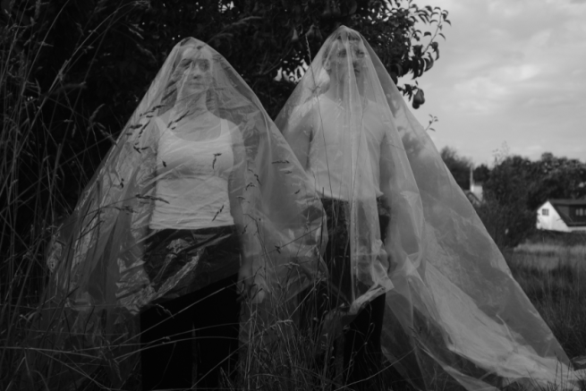 Two people stand in a field covered in a thick plastic sheet