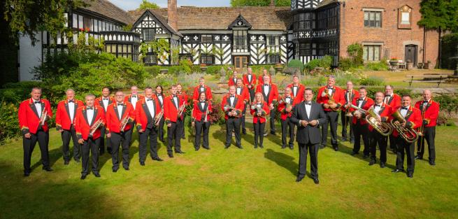 A brass band standing on the green lawn with a country house behind them.  