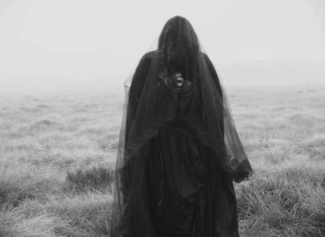 A black and white image of a banshee figure draped in dark fabric on a misty moor