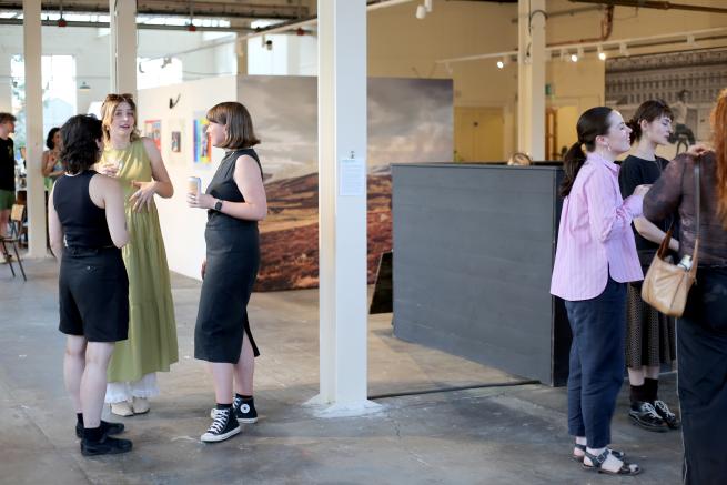 Two groups of people stand withing an industrial Gallery space surrounded by large photography pieces and instillations.