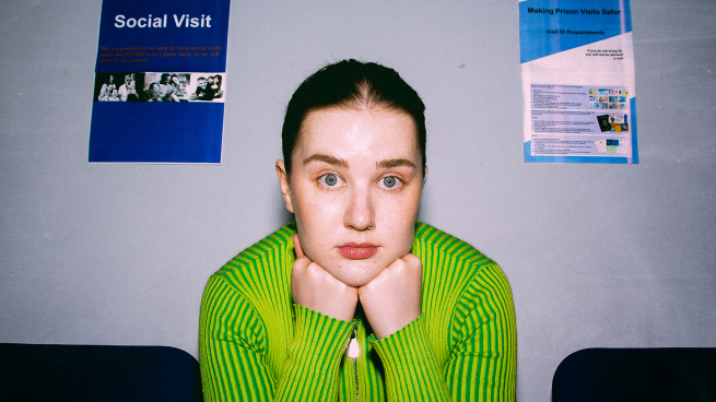 A young woman resting her head on her hands in a prison waiting room. 