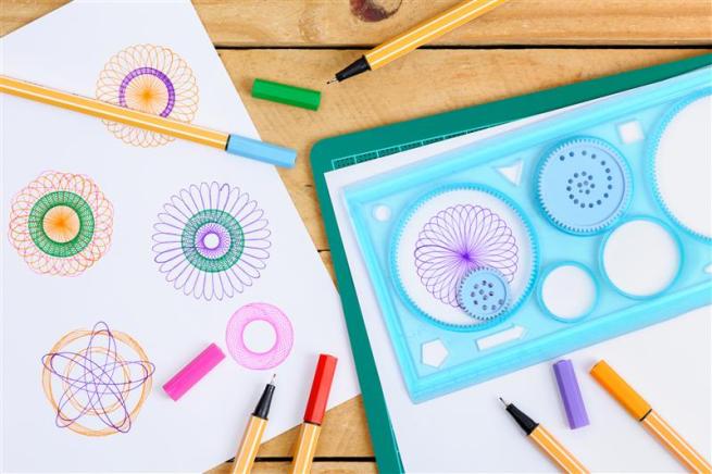 A photo of a spirograph on a table, alongside some pens and paper