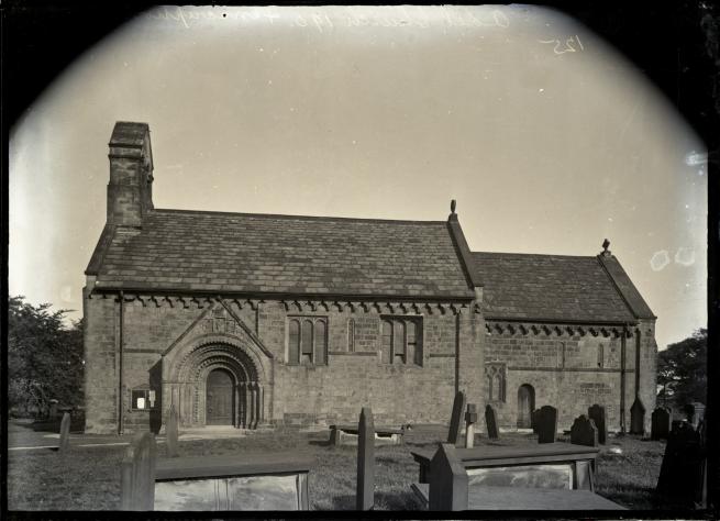 A black and white lantern slide view of a small church with Norman arched doorway (St John the Baptist, Adel, Leeds), set in a graveyard