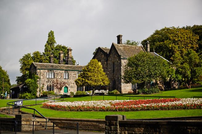 An image of a stone house (Abbey House Museum) on a hill, with flowerbeds and trees in the foreground.
