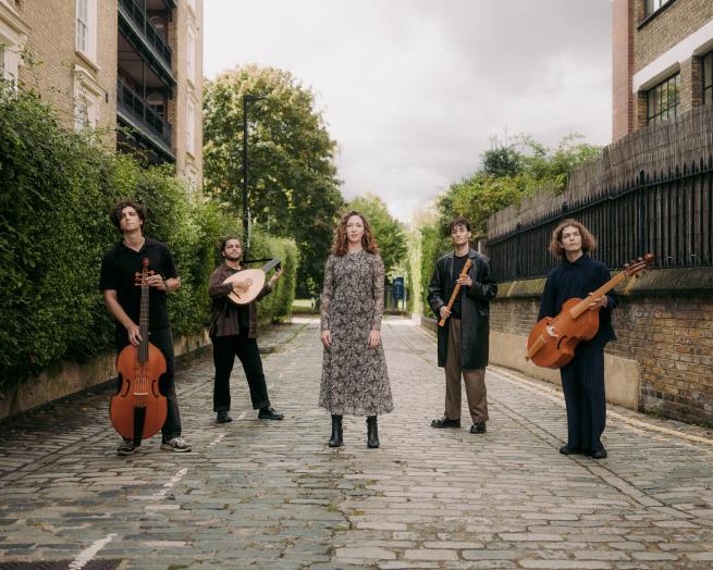 Five musicians stood in a street hold their instruments. 