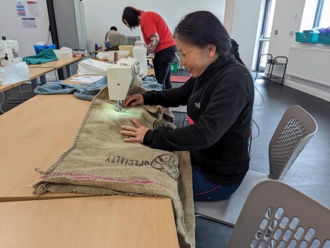 A women sat sewing a bag. 