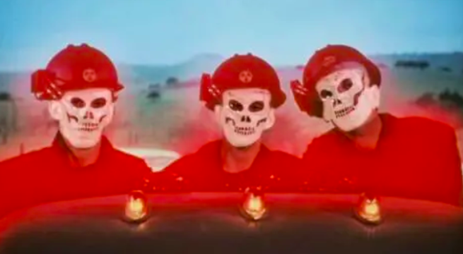 Still from Human Highway of three skeleton faces with red boilersuits and helmets on