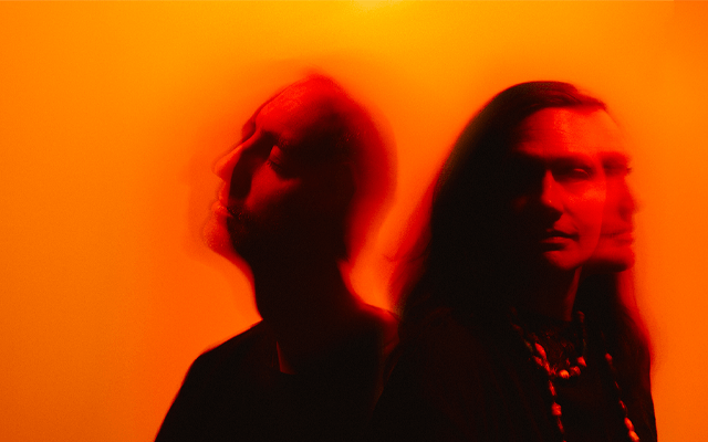 A surreal photograph with orange light, featuring two out of focus members of the Manchester Collective 