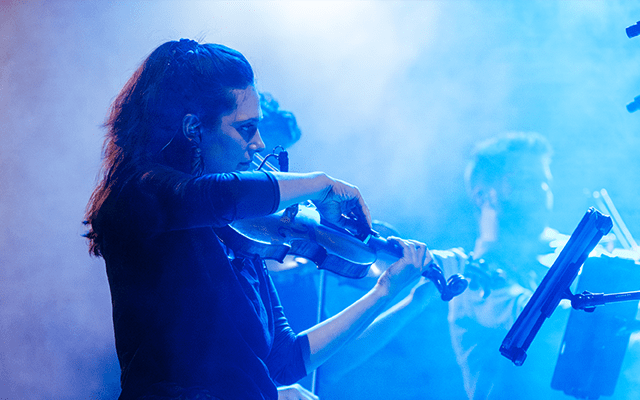 The Manchester Collective performing on stage; violin players playing together in foggy blue light