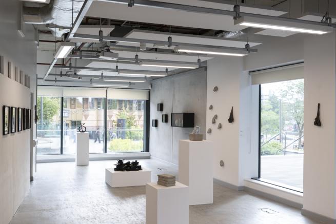 Installation image of Mia Mai Symonds' exhibition 'A Life if its Own' at BLANK_ gallery, Leeds. The photo shows small sculptural works both on walls and plinths with materials including, charred wood, bronze casts, framed images, ceramics and concrete. 
