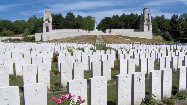 An image of Etaples Military Cemetery - white gravestones stand from the foreground to the horizon with the blue sky.