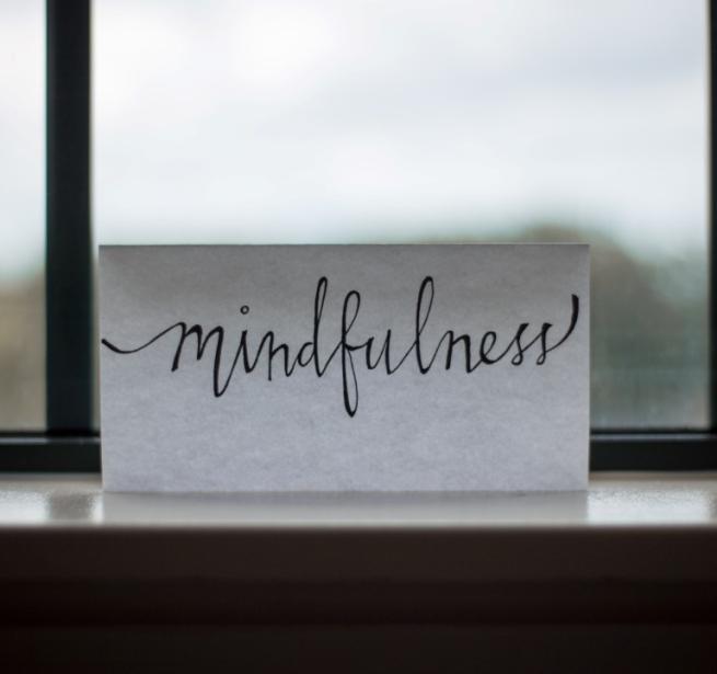 Mindfulness is written in script on a piece of paper and propped up on a windowsill.