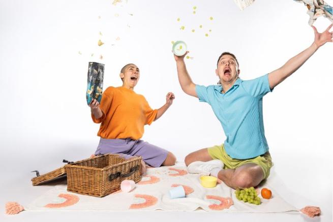 Two people on a picnic blanket throwing food in the air.