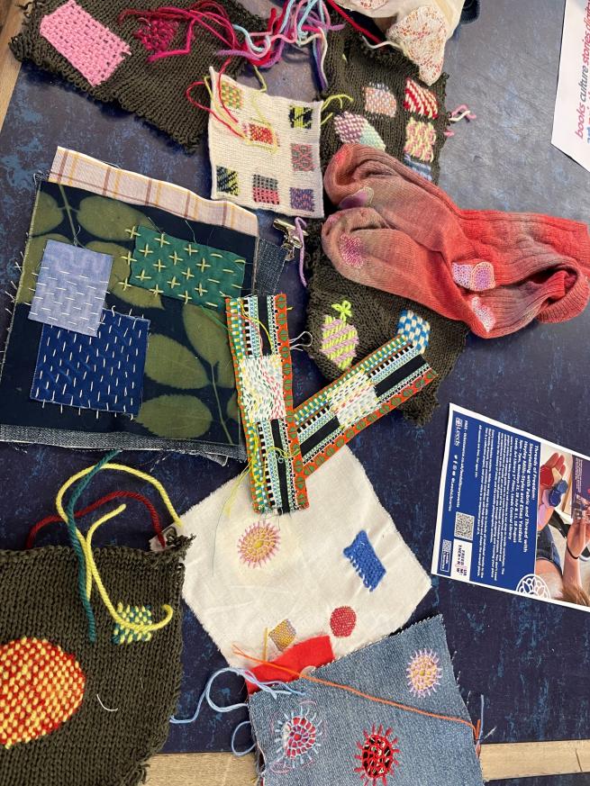 A table is strewn with patched up fabric, thread, in multiple colours. 
