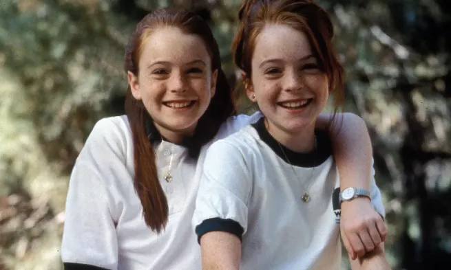 Two young girls who look remarkably similar smile at the camera. One has her arm across the other's shoulders.