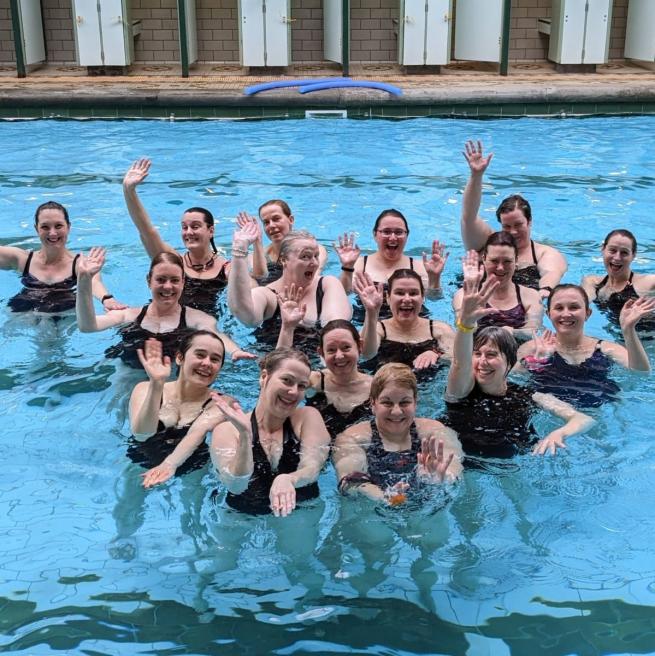 women in pool waving at camera