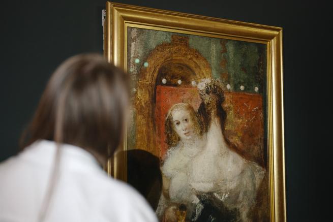 A woman gazes thoughtfully at a painting depicting another woman.