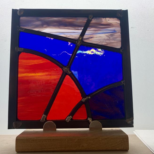 Handcrafted stained glass panel with colorful geometric shapes of blue, red and purple glowing in sunlight.