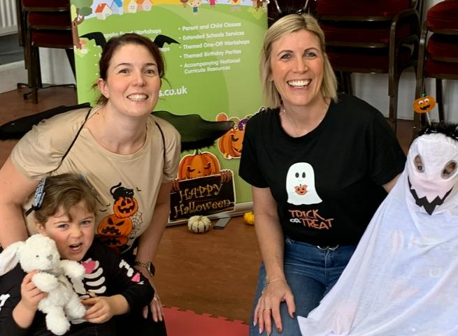 Two adult females in halloween t-shirts with two young children in halloween costume on their laps